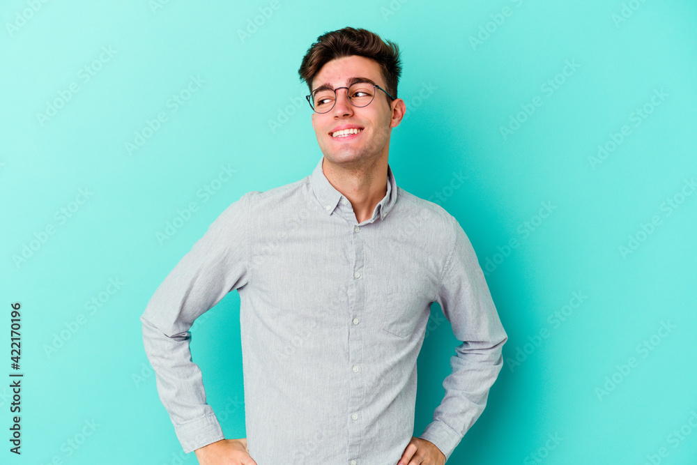 Young caucasian man isolated on blue background laughs happily and has fun keeping hands on stomach. Young caucasian man isolated on blue background laughs happily and has fun keeping hands on stomach.