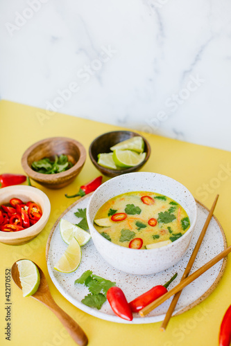 spicy thai coconut soup on a yellow background with chiles, lime and cilantro as garnish