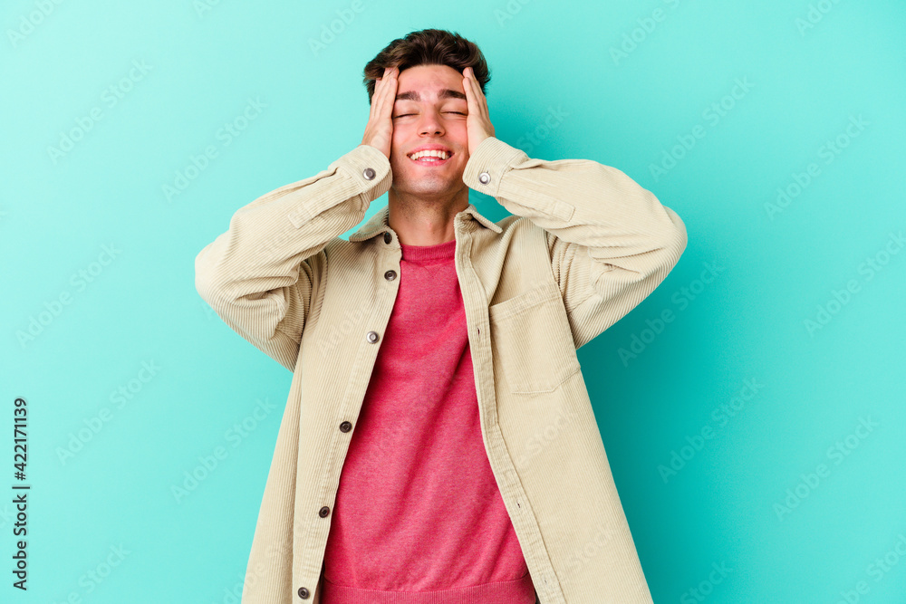 Young caucasian man isolated on blue background laughs joyfully keeping hands on head. Happiness concept.