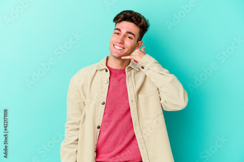 Young caucasian man isolated on blue background showing a mobile phone call gesture with fingers.