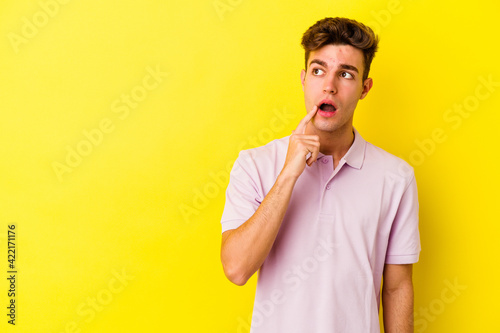 Young caucasian man isolated on yellow background looking sideways with doubtful and skeptical expression.