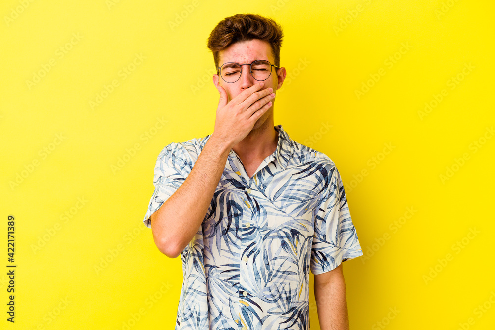 Young caucasian man isolated on yellow background yawning showing a tired gesture covering mouth with hand. Young caucasian man isolated on yellow background yawning showing a tired gesture covering mouth with hand.