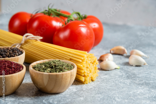 Raw spaghetti, spices and tomatoes on marble background