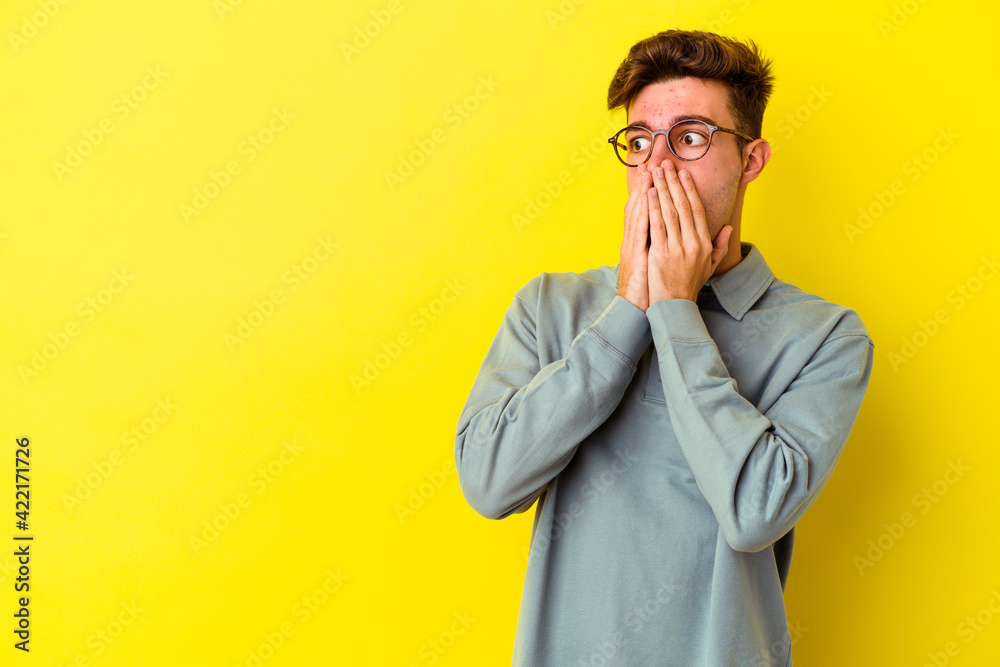 Young caucasian man isolated on yellow background thoughtful looking to a copy space covering mouth with hand. Young caucasian man isolated on yellow background thoughtful looking to a copy space covering mouth with hand.