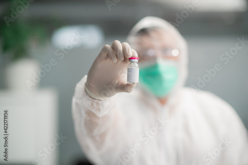 A medic in a protective suit holds a bottle of vaccine in his hands.