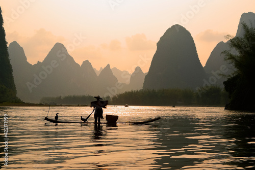 Cormorant fisherman on the Li River (Lijiang) with karst peaks in the background at sunset, near Xingping, Guangxi Province, China