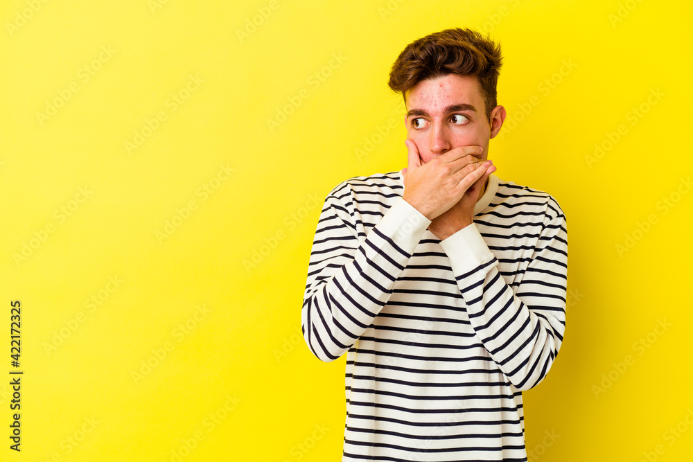 Young caucasian man isolated on yellow background thoughtful looking to a copy space covering mouth with hand. Young caucasian man isolated on yellow background thoughtful looking to a copy space covering mouth with hand.