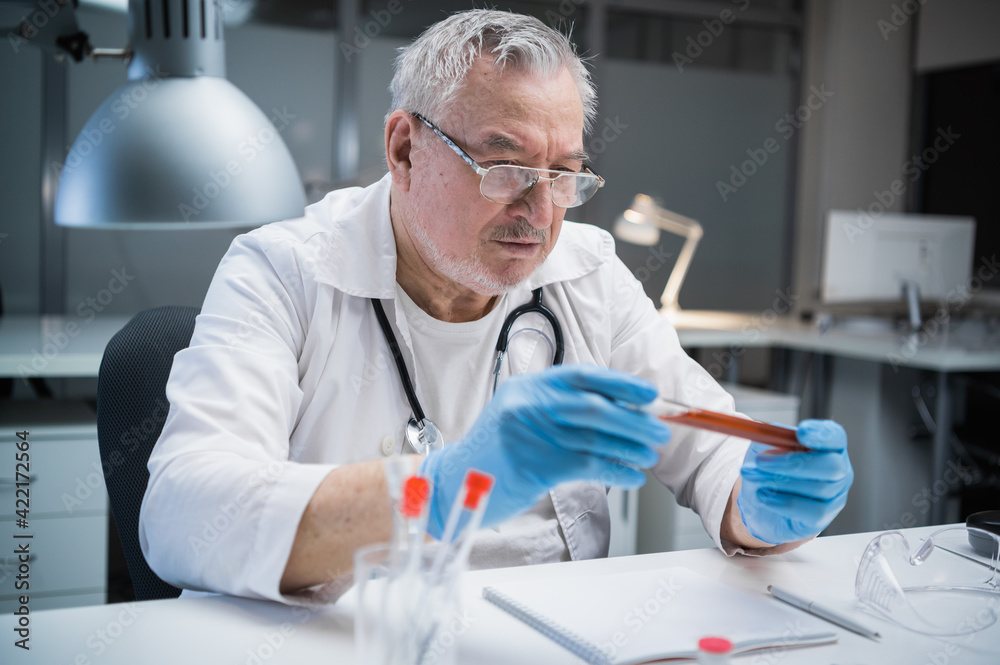 A medical laboratory assistant examines the properties of the vaccine produced. He holds a bottle with a blood sample containing a vaccine against the covid-19 virus. A medical laboratory assistant examines the properties of the vaccine produced. He holds a bottle with a blood sample containing a vaccine against the covid-19 virus.