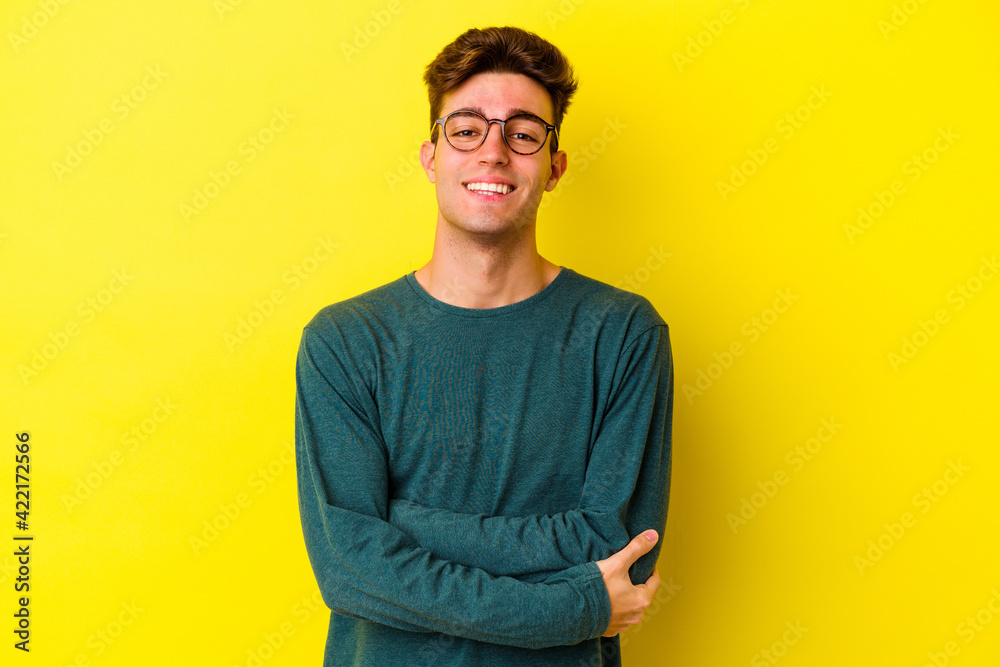 Young caucasian man isolated on yellow background who feels confident, crossing arms with determination. Young caucasian man isolated on yellow background who feels confident, crossing arms with determination.