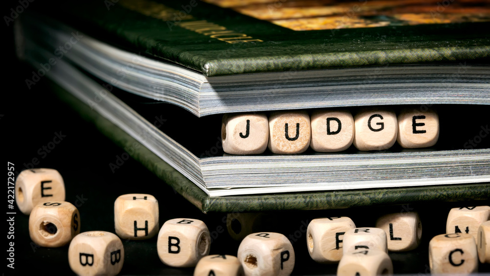 The word judge is written in wooden blocks in a green notebook on a black background, cubes are scattered in the foreground The word judge is written in wooden blocks in a green notebook on a black background, cubes are scattered in the foreground