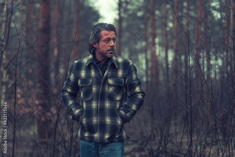 Middle aged man with stubble beard in a checkered coat in a rainy forest.