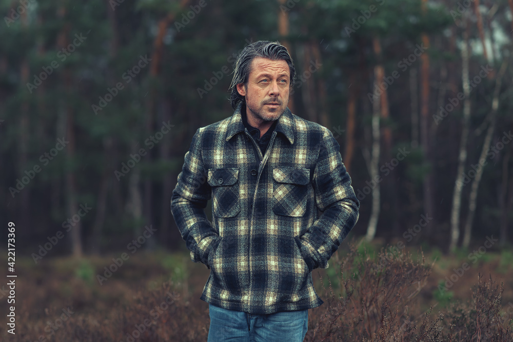 Middle aged man with stubble beard in a checkered coat in a rainy heathland.