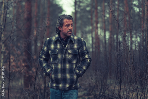 Middle aged man with stubble beard in a checkered coat in a rainy forest.