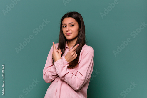 Young Indian woman isolated on blue background points sideways, is trying to choose between two options.
