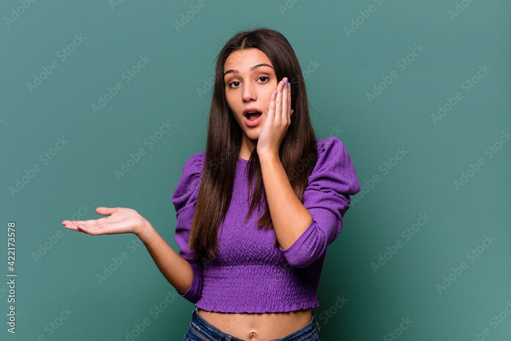 Young Indian woman isolated on blue background impressed holding copy space on palm. Young Indian woman isolated on blue background impressed holding copy space on palm.