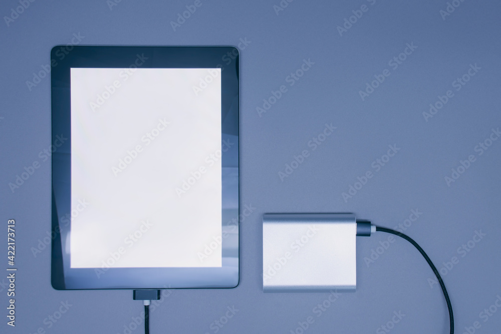Portable charger charges a mockup Tablet with white screen isolated on a gray background.