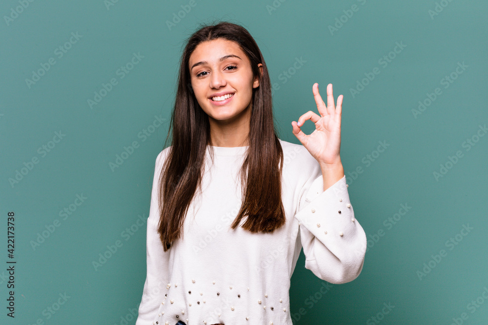 Young Indian woman isolated on blue background cheerful and confident showing ok gesture. Young Indian woman isolated on blue background cheerful and confident showing ok gesture.