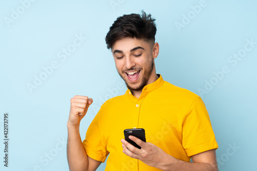 Arabian handsome man over isolated background with phone in victory position