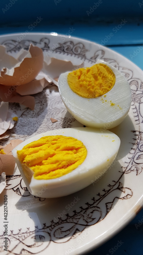 Closeup hard boiled egg sliced in halves and broken eggshell on retro crockery plate. Organic farm chicken egg cooked for breakfast. Healthy eating nutrition Closeup hard boiled egg sliced in halves and broken eggshell on retro crockery plate. Organic farm chicken egg cooked for breakfast. Healthy eating nutrition