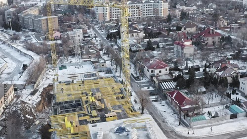 Construction site with yellow scaffolding and cranes - the construction of multi-storey apartment building in the residential quarter of the city. Construction cranes and workers doing work.