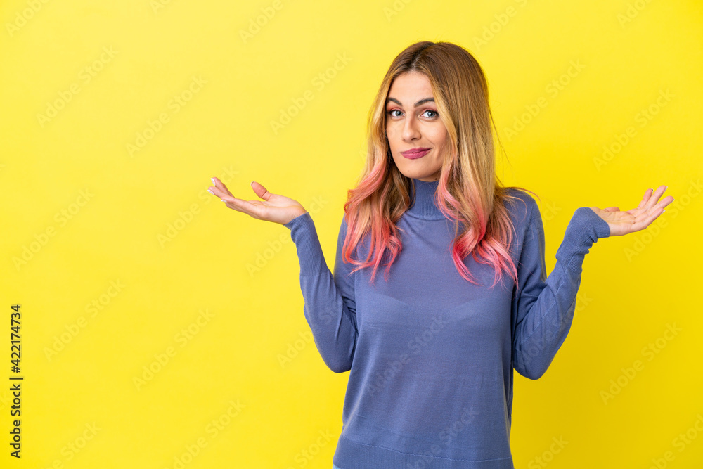 Young woman over isolated yellow background having doubts while raising hands Young woman over isolated yellow background having doubts while raising hands
