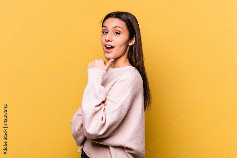 Young Indian woman isolated on yellow background points with thumb finger away, laughing and carefree. Young Indian woman isolated on yellow background points with thumb finger away, laughing and carefree.