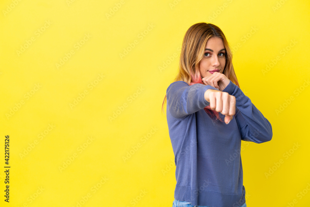Young woman over isolated yellow background with fighting gesture Young woman over isolated yellow background with fighting gesture