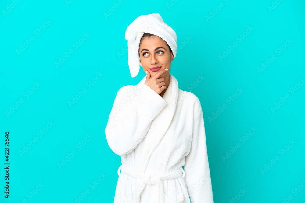 Young woman in a bathrobe over isolated blue background looking up while smiling Young woman in a bathrobe over isolated blue background looking up while smiling