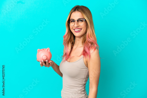 Young woman over isolated blue background holding a piggybank smiling a lot