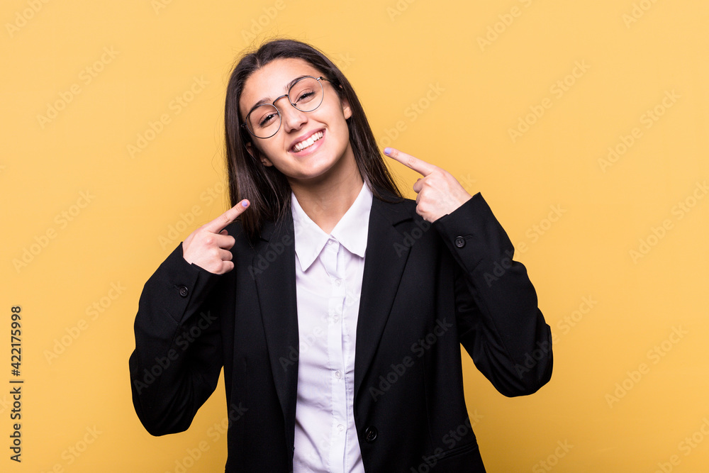 Young Indian business woman isolated on yellow background smiles, pointing fingers at mouth. Young Indian business woman isolated on yellow background smiles, pointing fingers at mouth.