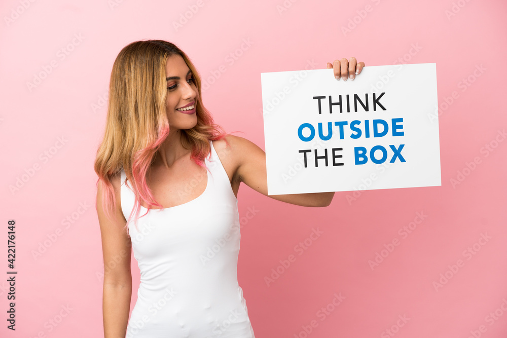 Young woman over isolated pink background holding a placard with text Think Outside The Box Young woman over isolated pink background holding a placard with text Think Outside The Box