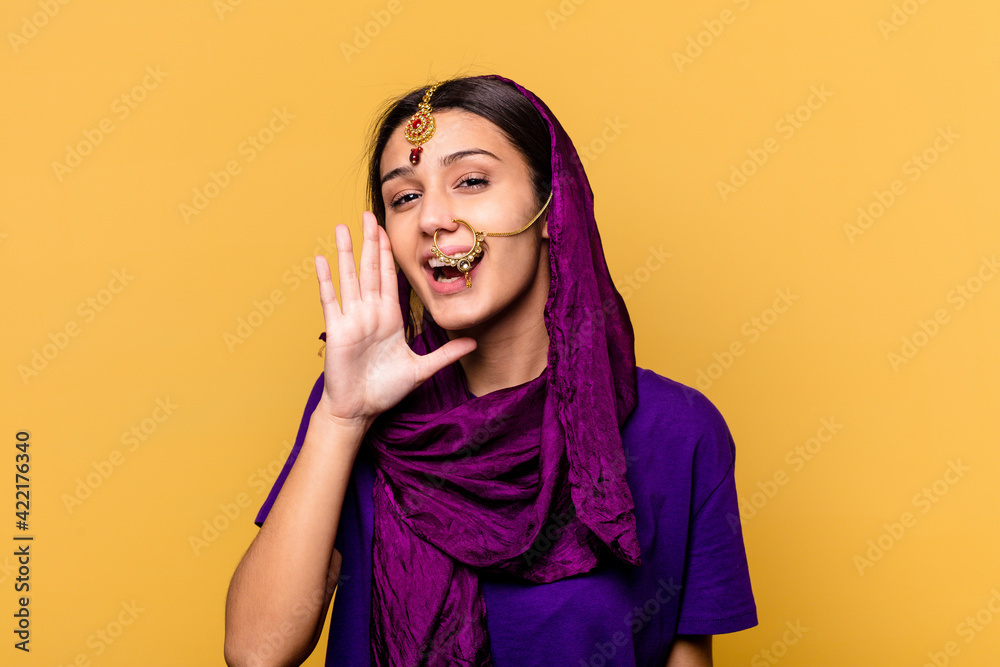 Young Indian woman wearing a traditional sari clothes isolated on yellow background shouting and holding palm near opened mouth. Young Indian woman wearing a traditional sari clothes isolated on yellow background shouting and holding palm near opened mouth.
