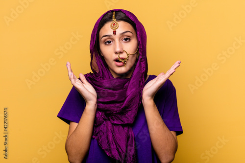 Young Indian woman wearing a traditional sari clothes isolated on yellow background surprised and shocked. © Asier