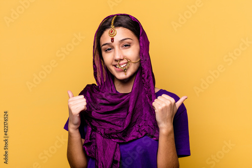 Young Indian woman wearing a traditional sari clothes isolated on yellow background raising both thumbs up, smiling and confident.