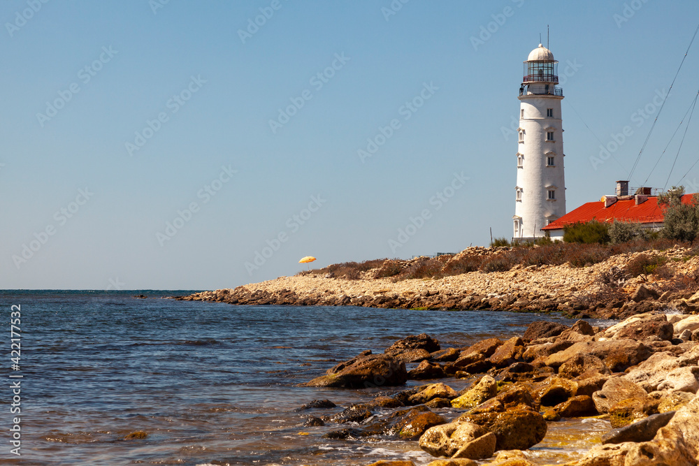 A tall white lighthouse stands on a rocky seashore