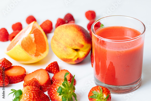 Red smoothie in a glass next to apricot, strawberries, grapefruit and raspberries. Red juice from fresh fruits. Healthy juice for breakfast. 