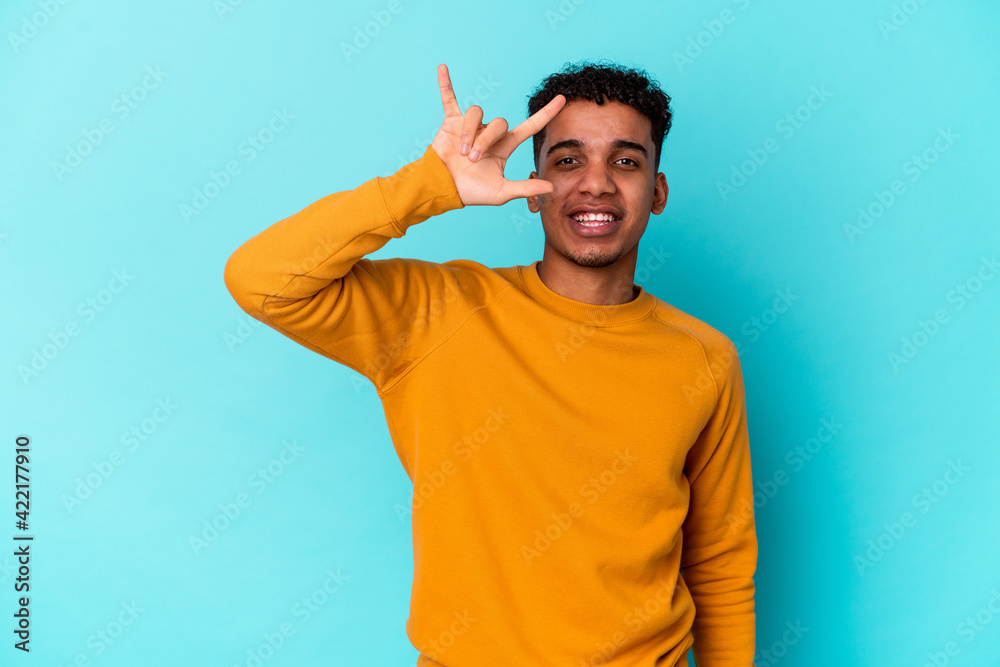 Fototapeta premium Young african american curly man isolated on blue showing a horns gesture as a revolution concept.