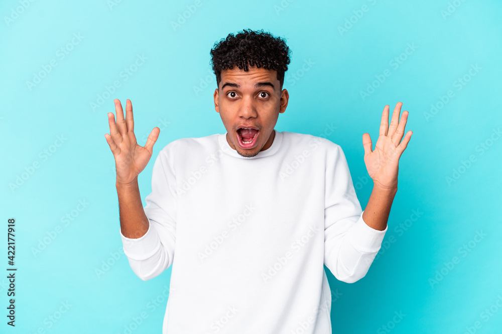 Young african american curly man isolated on blue celebrating a victory or success, he is surprised and shocked.