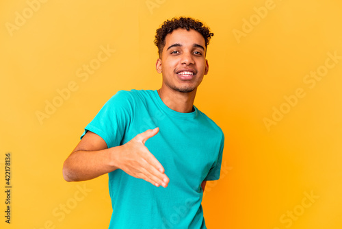 Young african american curly man isolated on purple stretching hand at camera in greeting gesture.