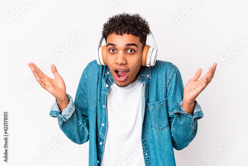 Young african american curly man isolated listening to music with headphones surprised and shocked.
