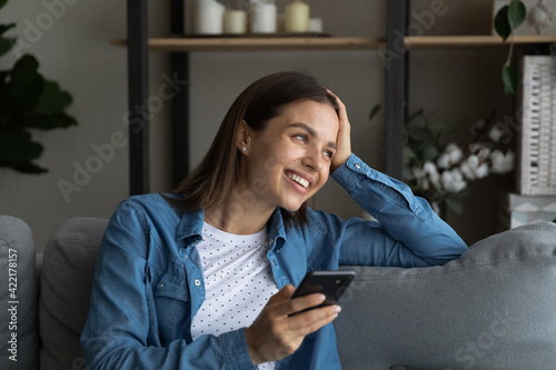 Close up smiling woman distracted from phone, sitting on couch, looking to aside, happy dreamy attractive female waiting for call, holding smartphone, dreaming about new opportunities, visualizing