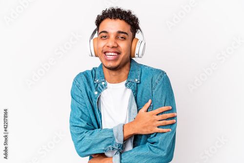 Young african american curly man isolated listening to music with headphones laughs out loudly keeping hand on chest.