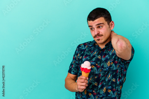 Young caucasian man eating an ice cream isolated on blue background touching back of head, thinking and making a choice.