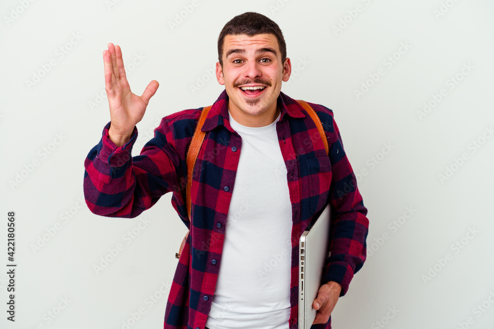 Young caucasian student man holding a laptop isolated on white background receiving a pleasant surprise, excited and raising hands. Young caucasian student man holding a laptop isolated on white background receiving a pleasant surprise, excited and raising hands.