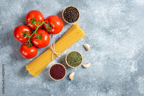 Raw spaghetti, spices and tomatoes on marble background