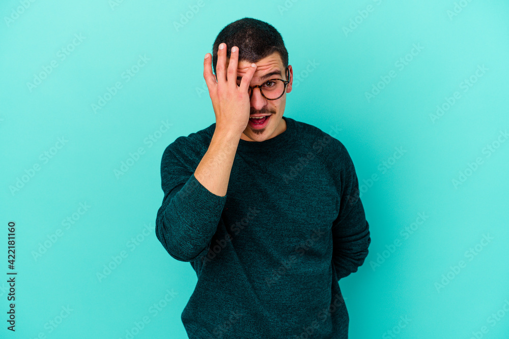 Young caucasian man isolated on blue background having fun covering half of face with palm. Young caucasian man isolated on blue background having fun covering half of face with palm.