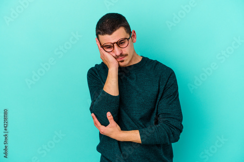 Young caucasian man isolated on blue background who is bored, fatigued and need a relax day.