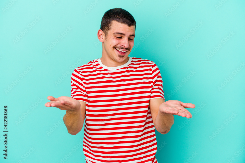 Young caucasian man isolated on blue background holding something with palms, offering to camera. Young caucasian man isolated on blue background holding something with palms, offering to camera.