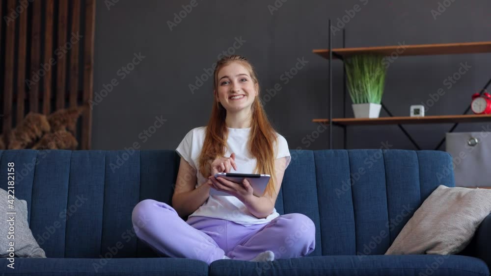 Beautiful Caucasian female sitting on sofa and using digital tablet in living room. Good-looking young woman holding gadget and looking at camera at home. Technology, lifestyle concept. Beautiful Caucasian female sitting on sofa and using digital tablet in living room. Good-looking young woman holding gadget and looking at camera at home. Technology, lifestyle concept.