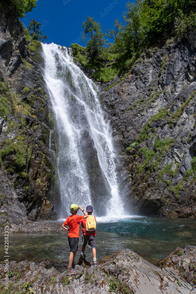 two adventurous children contemplate a large waterfall on a hike, Saut deth Pish in the Aran Valley,